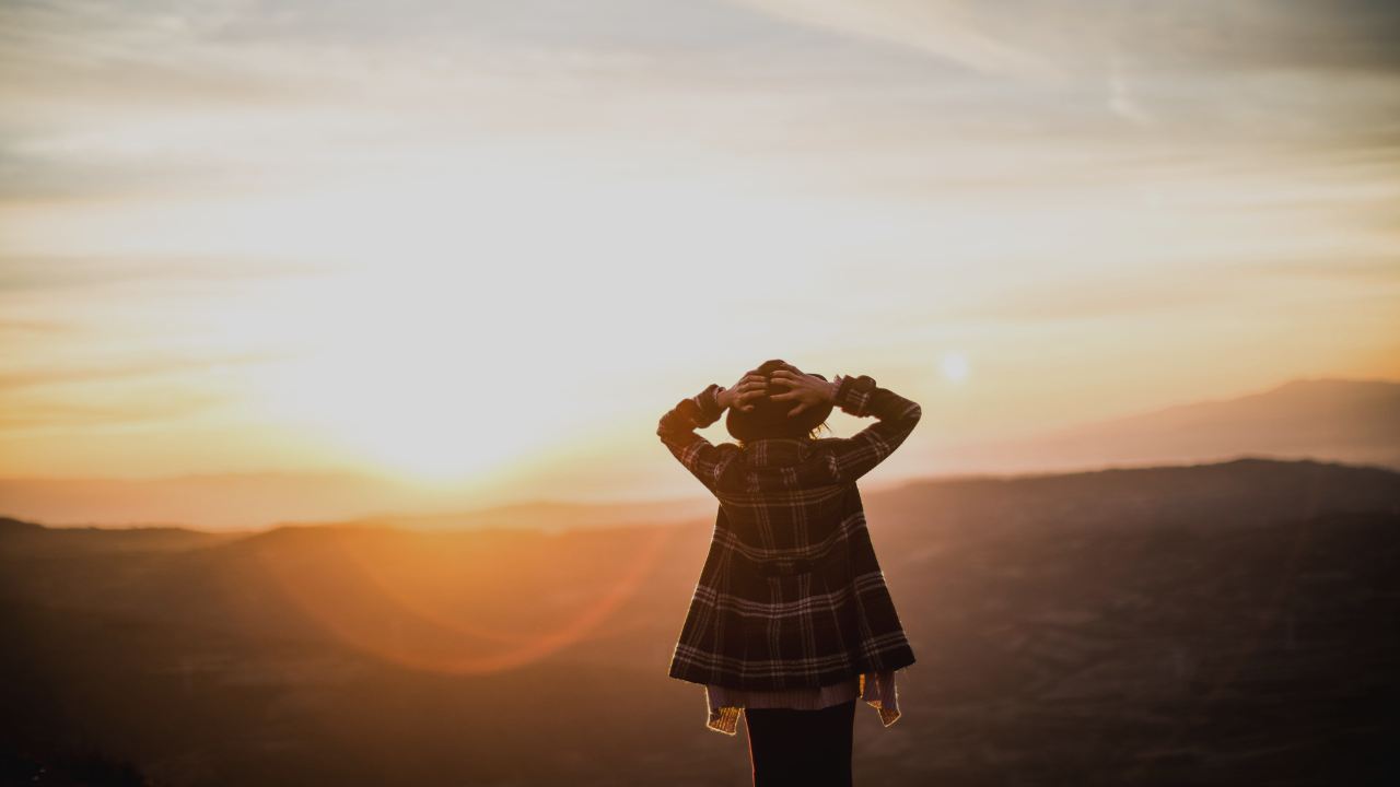 Mulher olhando o horizonte com o sol - realizando uma jornada interior